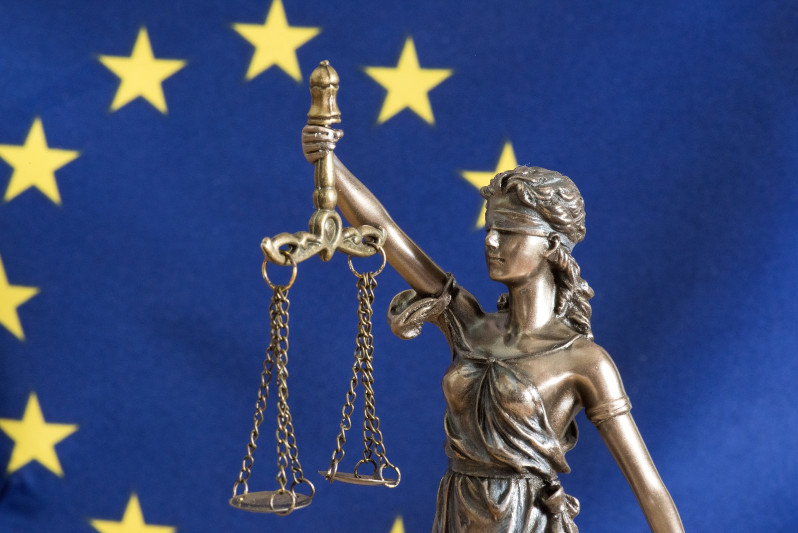 Bronzene Justitia-Statuette mit Waage und Augenbinde vor der Flagge der Europäischen Union